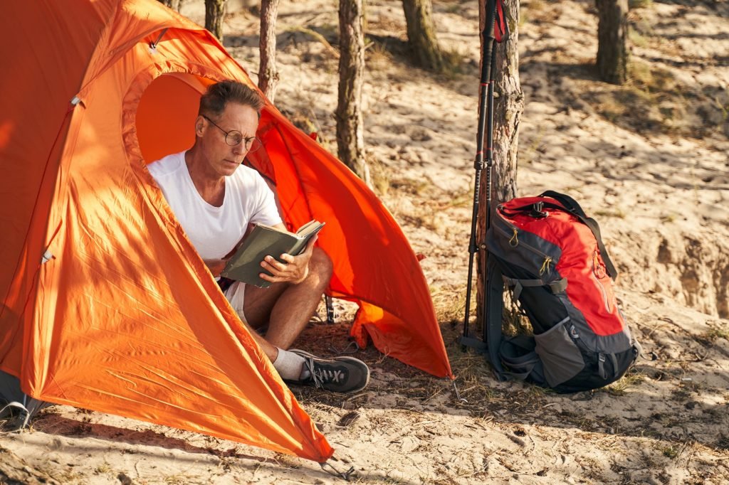 Calm male relaxing with book in tent in nature